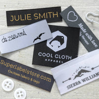 Black, white and gray woven labels with gold lettering, a heart outline and a Cool Cloth Apparel logo on pale wood.