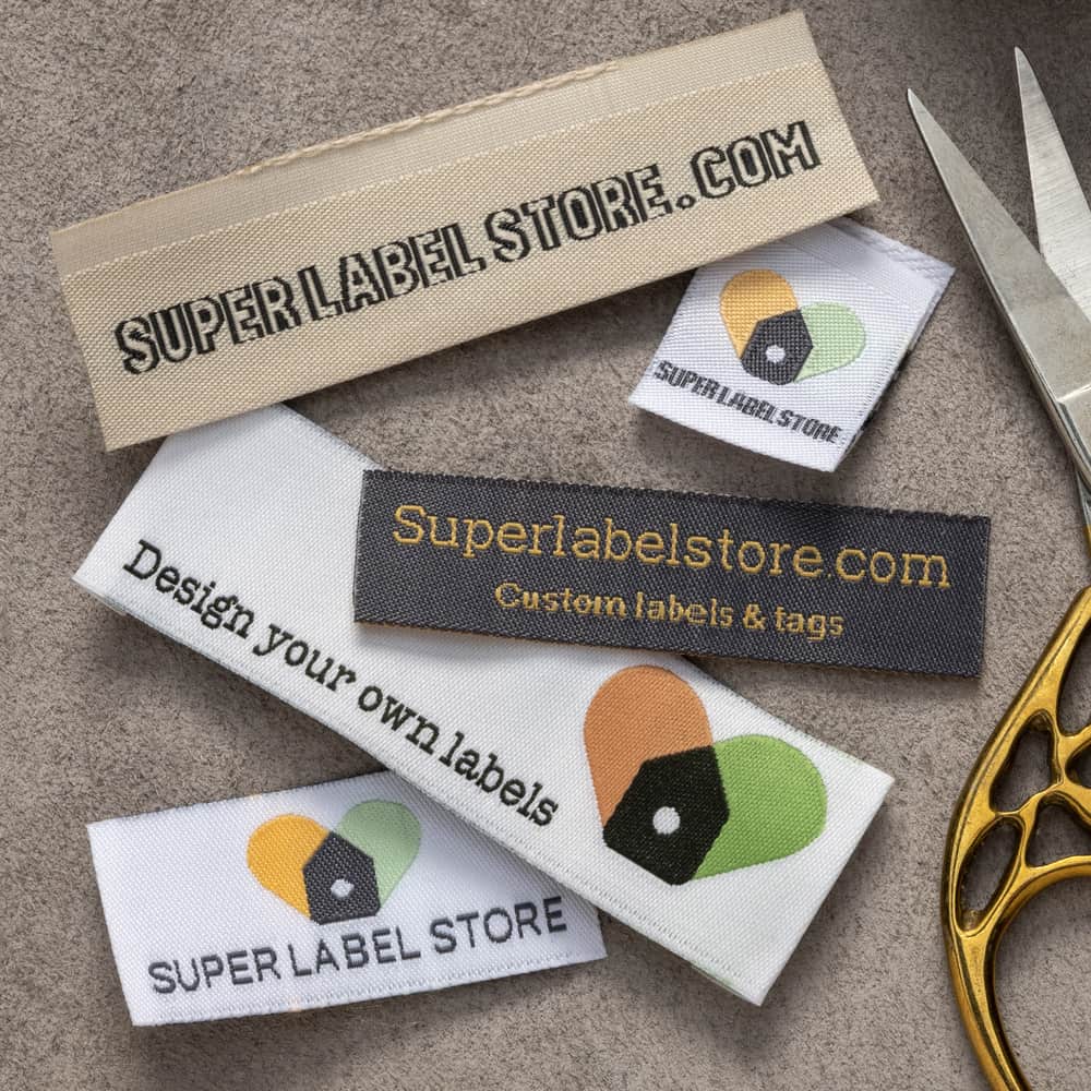 Cream, white and charcoal Super Label Store fabric labels with woven lettering and colored tag logos beside scissors.