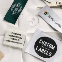 Green and white woven label samples on pattern paper, including a leafy hotel logo and a circular Custom Labels badge.