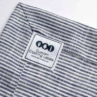White square woven label with a black border and cutlery logo, stitched onto navy and white striped fabric.