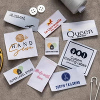 Assorted white fabric labels with Hand Sewn, Queen and Curtin Tailoring designs on a textured sewing surface.